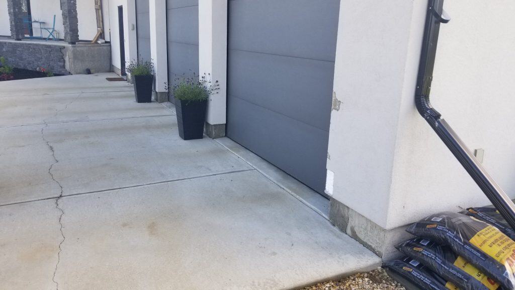 Driveway with visible concrete surface and garage door, featuring potted plants and construction materials, illustrating stucco repair context.