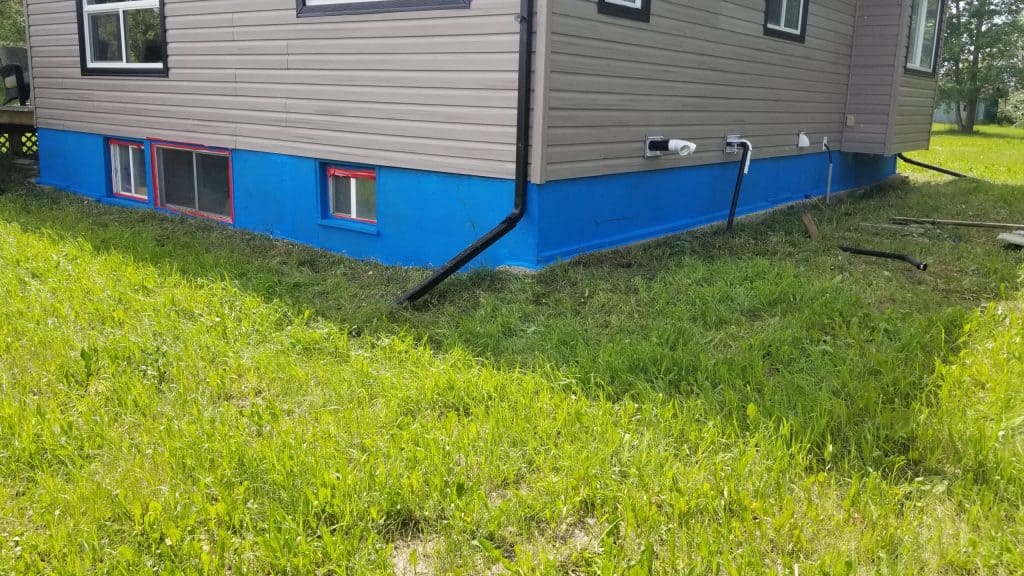 Exterior view of a building showcasing blue parging at the foundation, with visible drainage pipes and windows, emphasizing moisture prevention strategies for insulated concrete forms (ICF).
