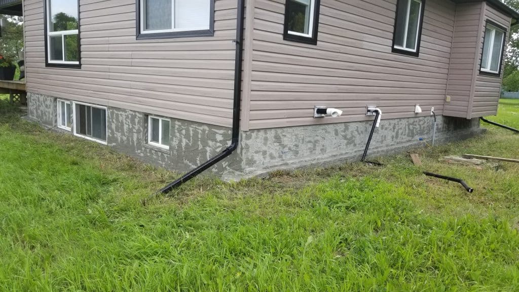 ICF home exterior showcasing parging application, drainage pipes, and window openings, emphasizing moisture prevention strategies.