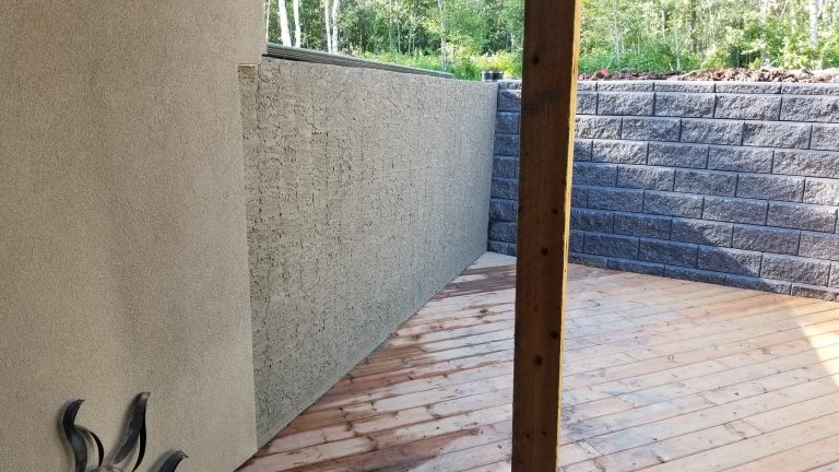 Parged foundation wall with textured finish beside a wooden deck, showcasing durable surface treatment for moisture protection and aesthetic appeal.