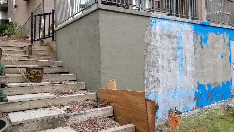 Parged foundation wall with smooth gray finish, adjacent to wooden steps and landscaping, illustrating the aesthetic enhancement and preparation for paint or color finishes.