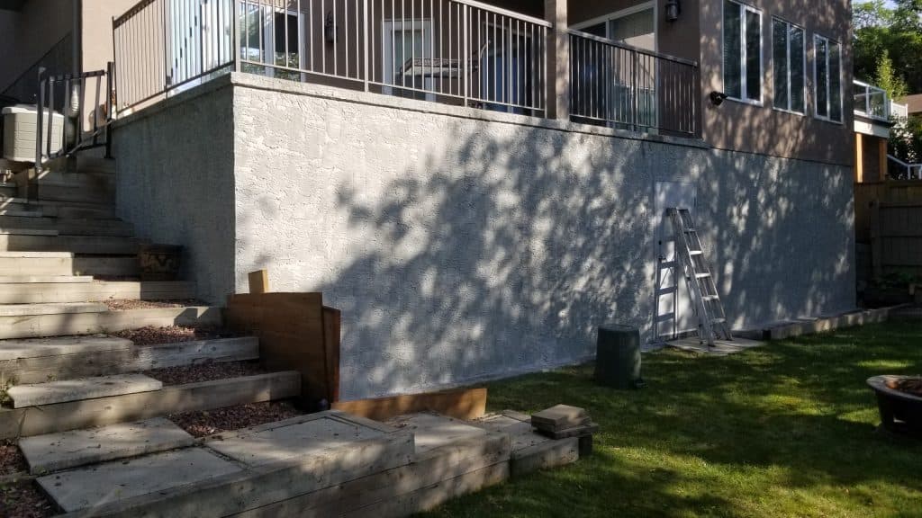 Parged exterior wall of a residential building, showcasing enhanced thermal performance and aesthetic appeal, with a ladder and landscaping elements in the foreground.