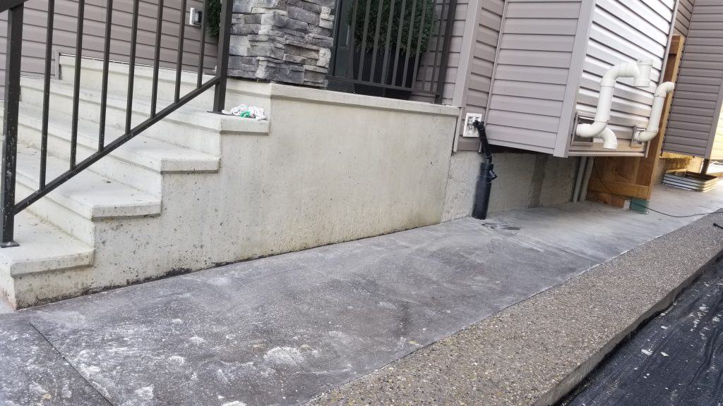 Concrete steps and foundation wall adjacent to a building, illustrating the application of cement parging for structural repair and aesthetic enhancement.