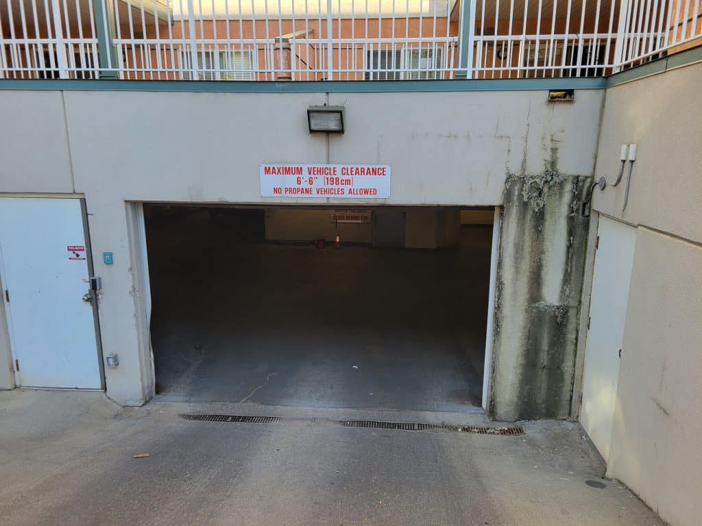 Maximum vehicle clearance sign indicating 6'6" height limit and prohibition of propane vehicles at stucco building entrance.