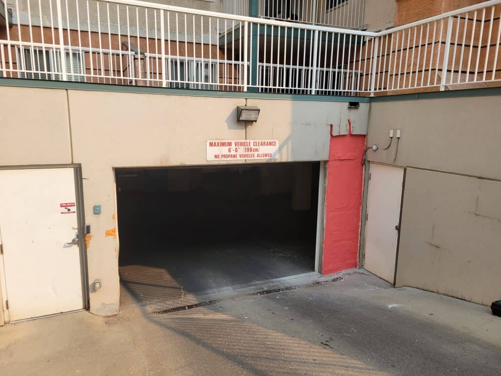 Entrance to a parking garage with a maximum vehicle clearance sign stating "6' 6" (198 cm)" and "No propane vehicles allowed," featuring a partially visible door and a red wall section.