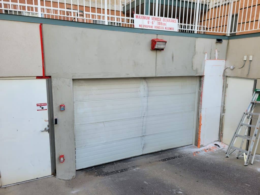 Stucco wall with garage door, visible repair area, and maintenance ladder, illustrating stucco repair services offered by Solida Coatings.