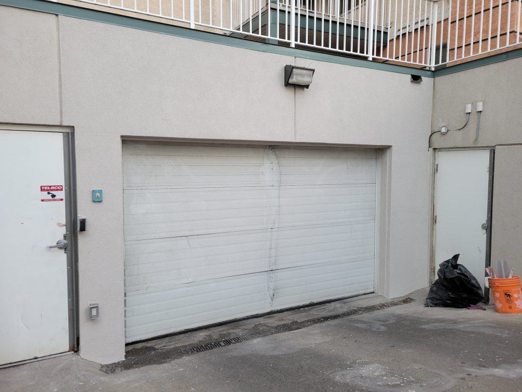 Stucco wall with a garage door and side entrance, showcasing potential areas for stucco restoration and retrofitting services by Solida Coatings Ltd.