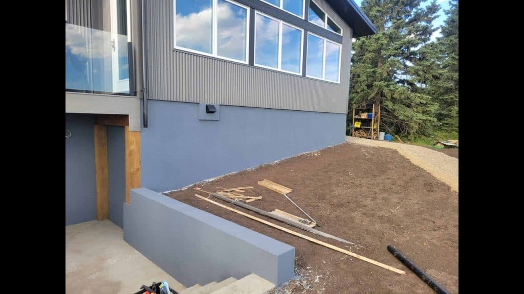 Parging installation on foundation wall of modern home in Edmonton, showcasing smooth textured finish and surrounding construction materials.