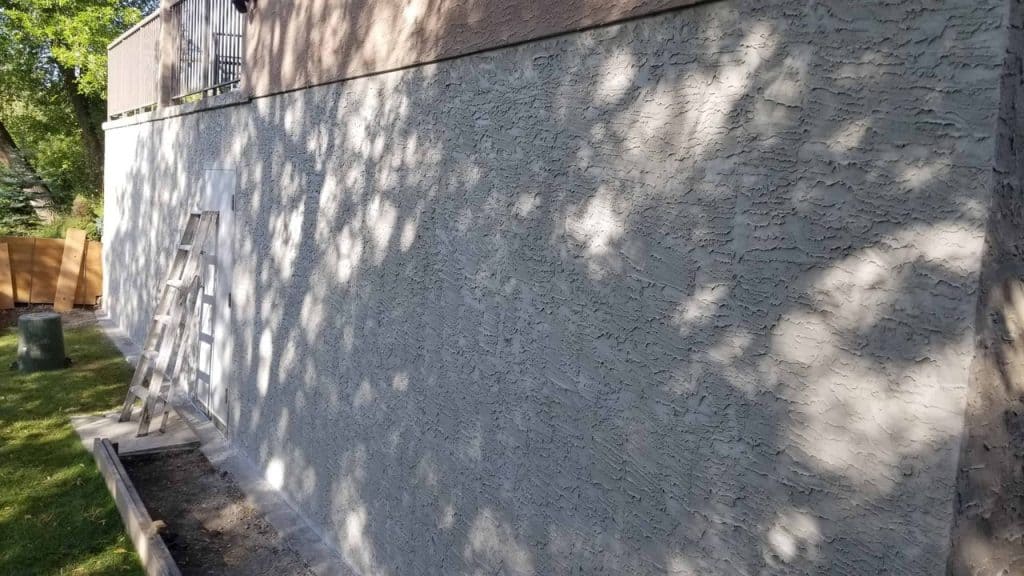 Parging installation on a foundation wall, showcasing textured coating with ladder and tools nearby, emphasizing professional parging services by Solida Coatings for foundation protection and aesthetics.