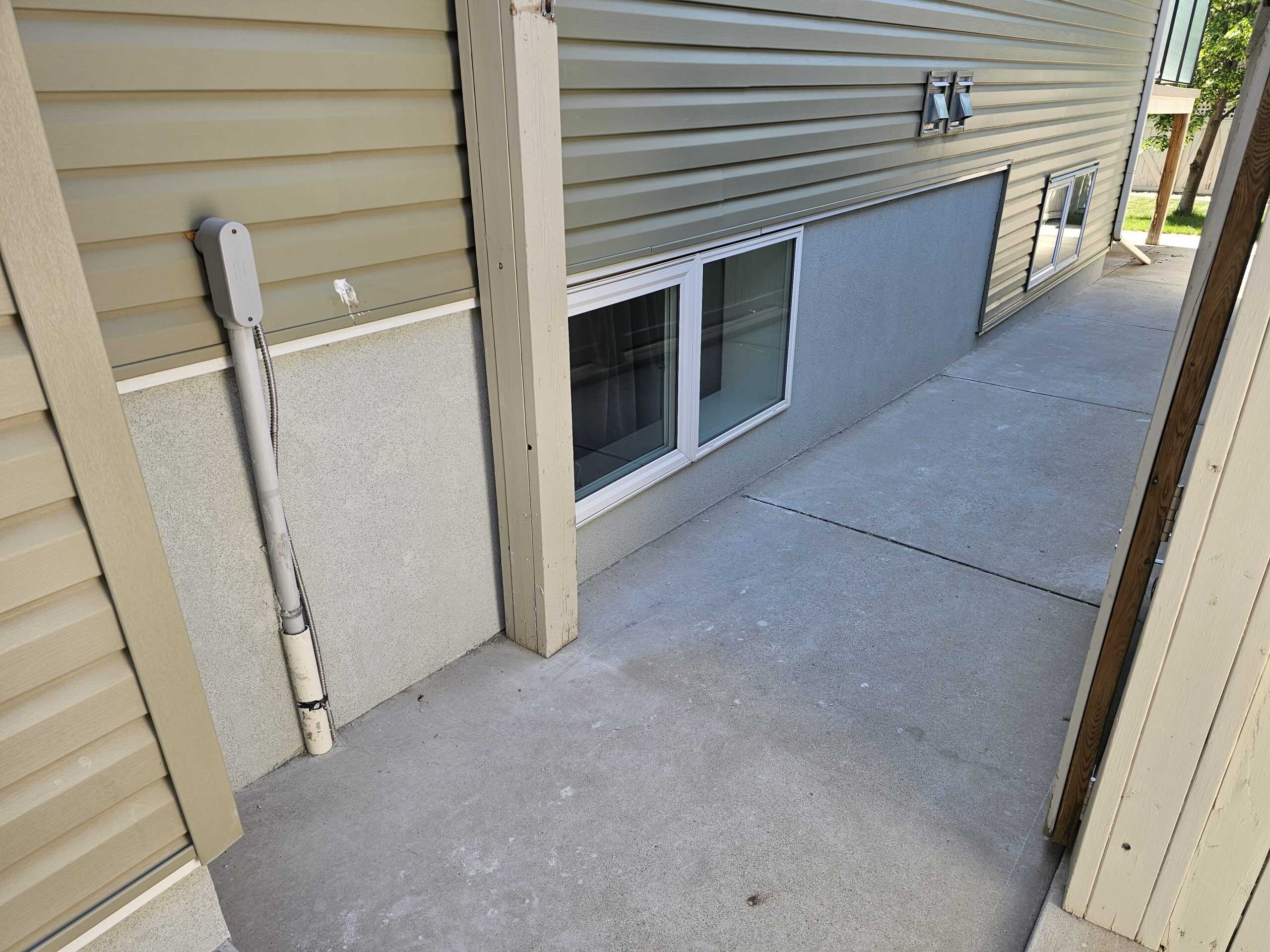 Parging-coated foundation wall with adjacent concrete pathway and utility conduit, illustrating effective moisture protection and aesthetic enhancement for residential properties.
