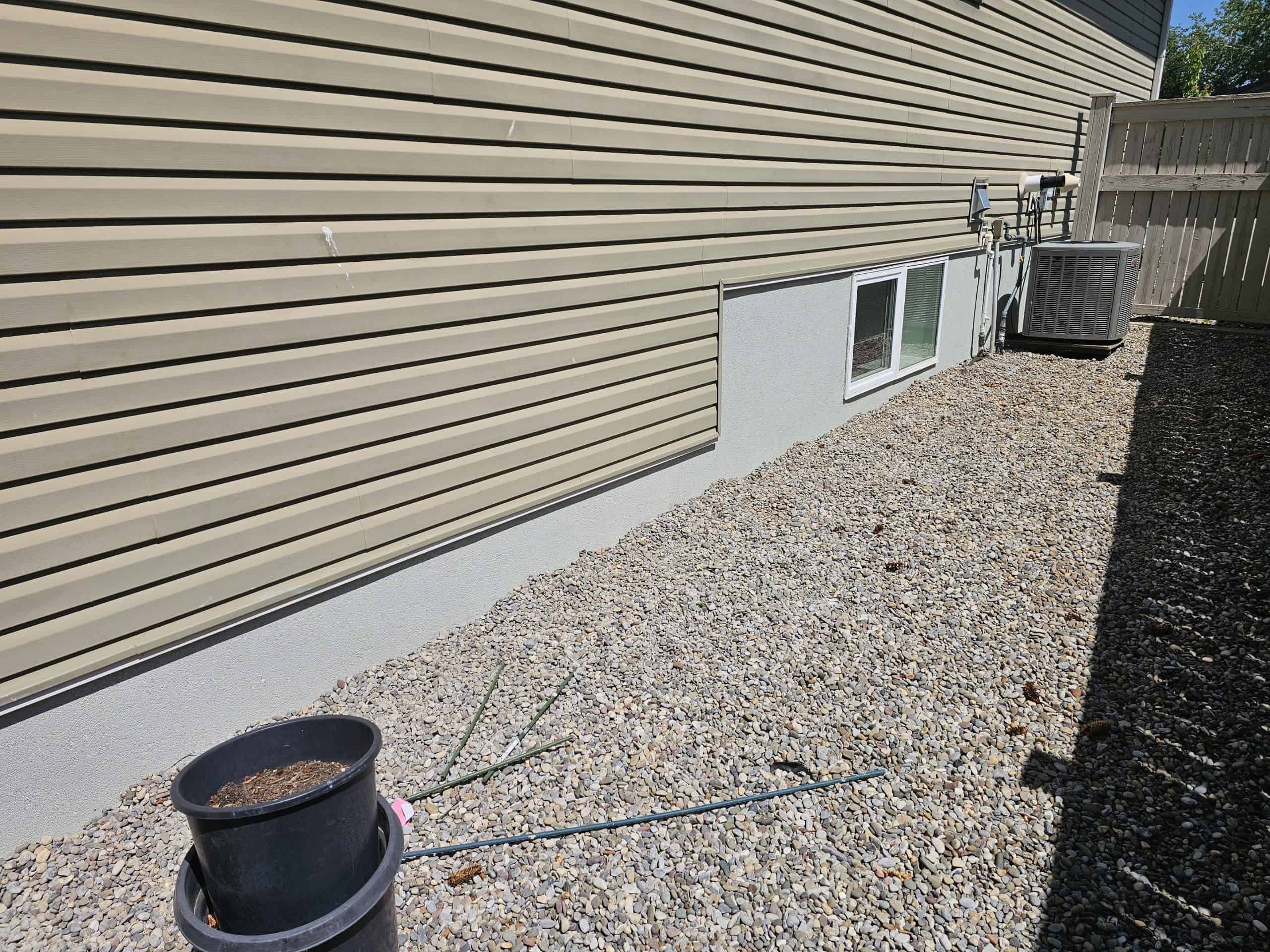 Parging applied to foundation wall with smooth surface, gravel landscaping, and adjacent air conditioning unit, illustrating foundation protection and moisture management.